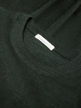 Close-up of a dark forest green knit crewneck sweater showing the ribbed collar and a small white fabric brand tag.