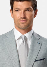 Man wearing a green checkered suit with a white shirt and gray tie on a light gray background