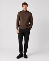 A man modeling a brown quarter-zip mock neck sweater and black trousers against a light gray studio background.