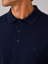 Close-up of a man wearing a navy blue ribbed knit polo shirt with a three-button placket and a small embroidered logo on the chest.