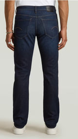 Person wearing dark blue jeans on a plain background