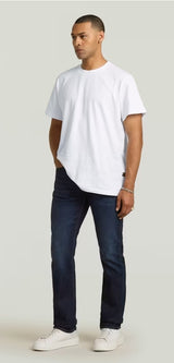 Man wearing a white t-shirt and dark jeans on a plain background
