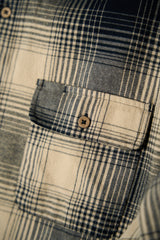 Close-up of a plaid flannel shirt pocket with a cream and navy check pattern and a single wooden button.