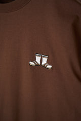 Close-up of a brown crewneck sweatshirt featuring a small embroidered pair of white socks with black and gold stripes on the left chest.
