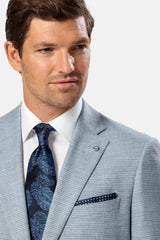 Man wearing a light blue suit with a blue patterned tie and pocket square on a white background