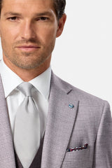 Man wearing a blush checkered suit with a white shirt and patterned tie on a light gray background