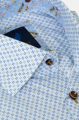 Close-up of a light blue patterned shirt with small navy and yellow dots, a floral print collar, and brown buttons.