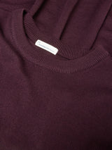 Close-up of a ribbed knit crewneck sweater in a deep plum purple color, showing the collar and a small white interior brand tag.