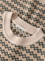 Close-up of a knitted sweater showing a cream ribbed crew neck collar and a geometric Fair Isle pattern in gray, cream, and orange.