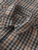 Close-up of a textured woven fabric with a geometric houndstooth-like pattern in navy, beige, and rust brown, showing part of a black zipper and collar.