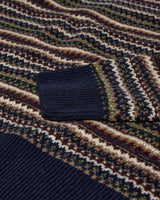Close-up of a knitted sweater showing a dark navy ribbed cuff and hem, with a multicolor Fair Isle pattern in navy, beige, brown, and green.