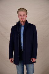 Man wearing a dark blue coat over a light blue shirt and jeans on a beige background