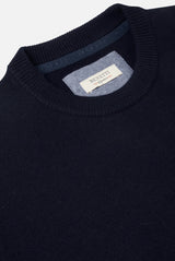 Navy sweater with a brand label on the collar against a light gray background