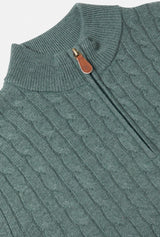 Teal cable knit sweater with a leather patch on a light gray background