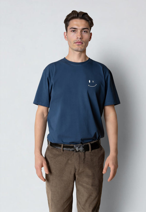Man wearing a navy blue t-shirt with a small smiley face logo on a plain background