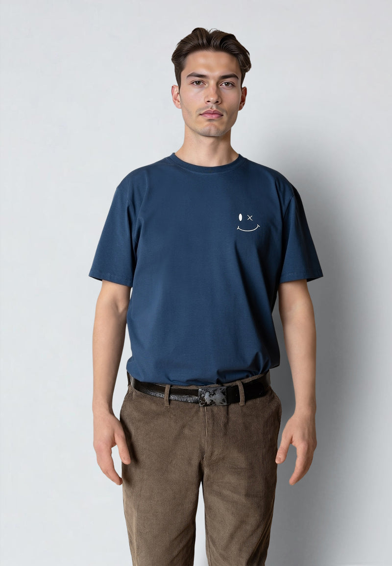 Man wearing a navy blue t-shirt with a small smiley face logo on a plain background