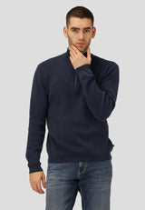 Man wearing a navy sweater and jeans against a plain background