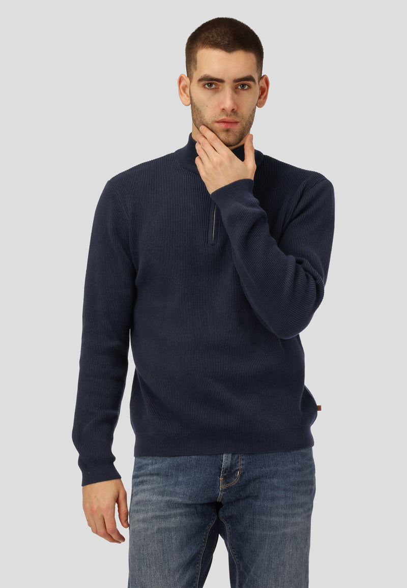 Man wearing a navy sweater and jeans against a plain background