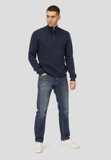 Man wearing a navy blue quarter-zip sweater and jeans on a light gray background