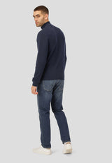 Man wearing a navy sweater and jeans on a light gray background