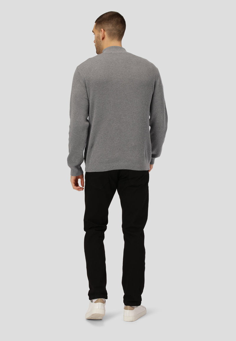 Man wearing a gray sweater and black pants on a light gray background