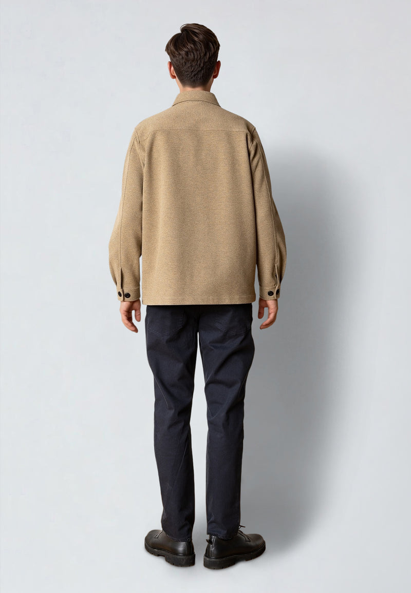 Person wearing a beige jacket and dark pants on a white background