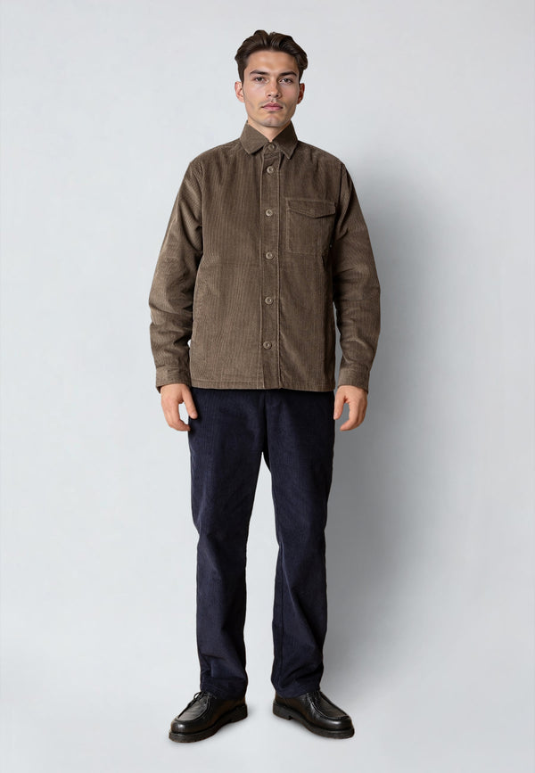 Man wearing a brown corduroy shirt and dark pants on a white background