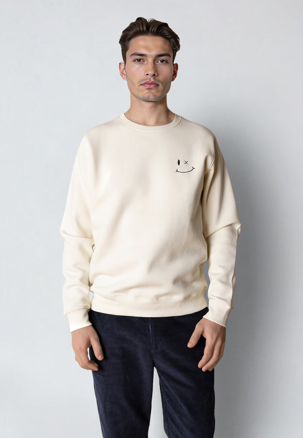 Man wearing a beige sweatshirt with a small graphic on a plain background