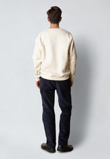 Person wearing a beige sweater and dark pants on a plain background