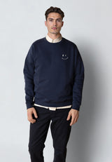 Man wearing a navy blue sweatshirt with a smiley face design on a plain background