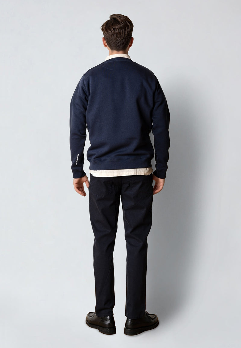 Man wearing a navy blue sweatshirt and black pants against a white background
