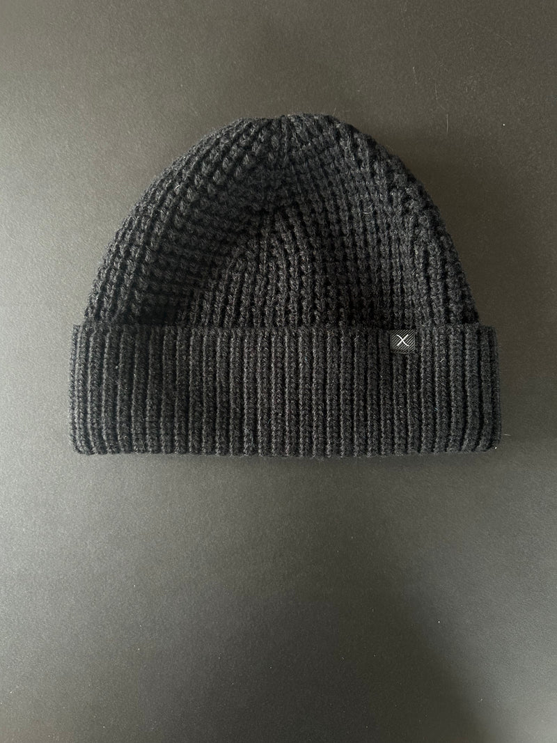 Black knit beanie with a brand logo on a matching gray background