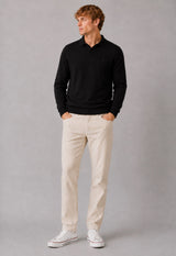 A man wearing a black long-sleeve polo shirt, beige trousers, and white sneakers, standing against a neutral gray studio background.