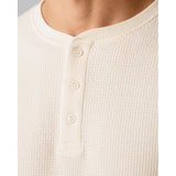 Close-up of a person wearing a waffle-knit henley shirt in a warm off-white or cream color, featuring a three-button placket.