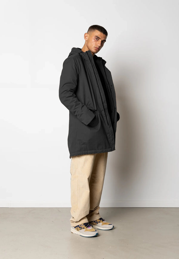 Man wearing a black coat, beige pants, and colorful sneakers against a white background
