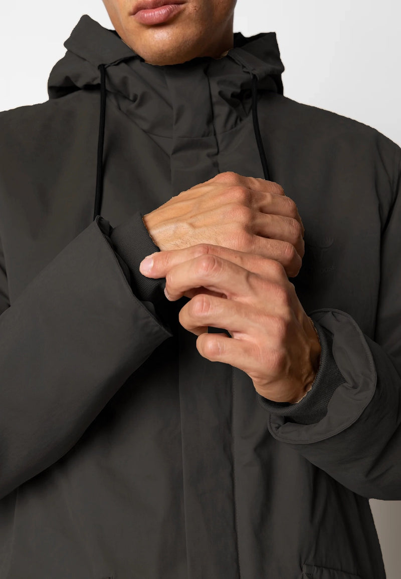Person wearing a black coat with a hood, holding their hands together.