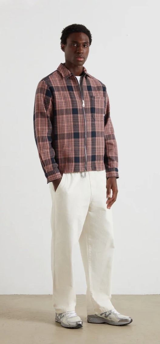 Person wearing a plaid overshirt and white pants against a plain background