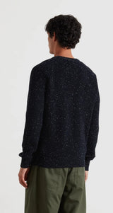 Person wearing a dark blue knitted sweater and green pants on a white background