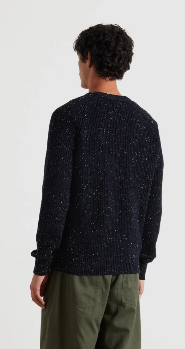 Person wearing a dark blue knitted sweater and green pants on a white background