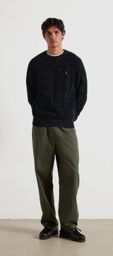 Man wearing a dark sweater and green pants against a white background