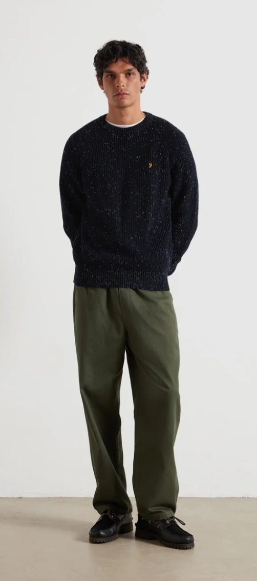 Man wearing a dark sweater and green pants against a white background
