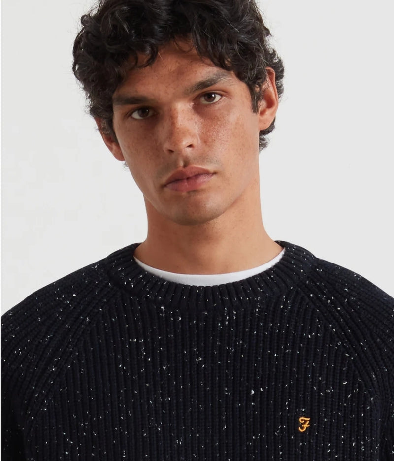 Man wearing a navy speckled sweater with a brand logo on a white background