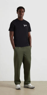 Person wearing a black t-shirt with a logo and green pants on a white background
