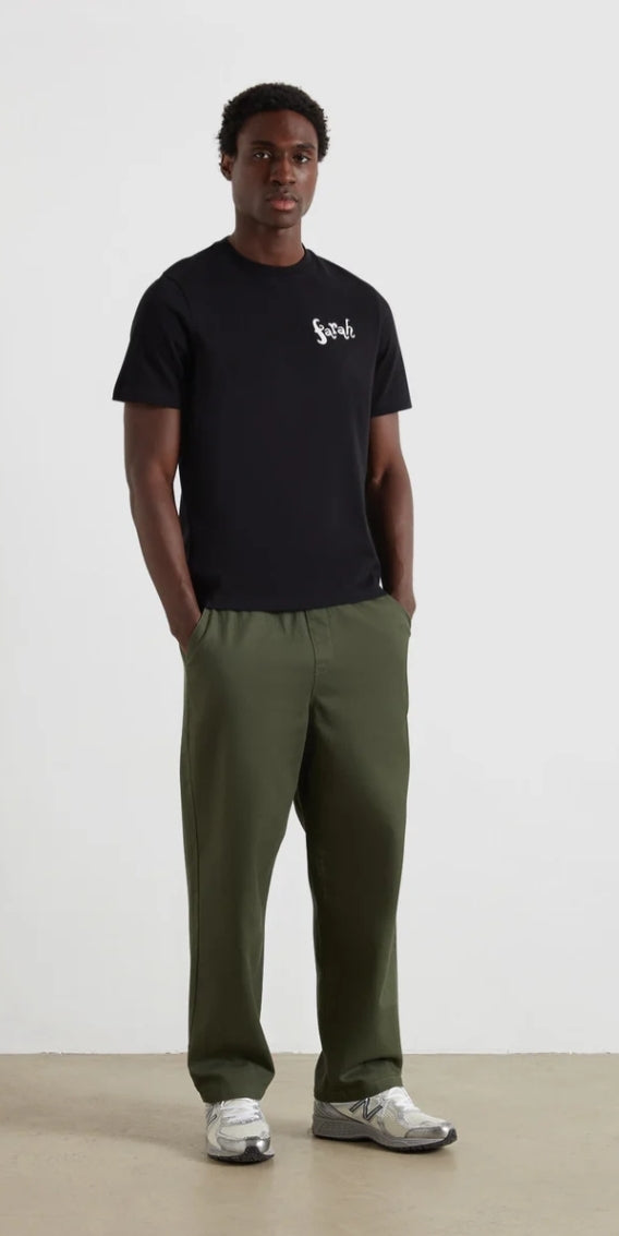 Person wearing a black t-shirt with a logo and green pants on a white background
