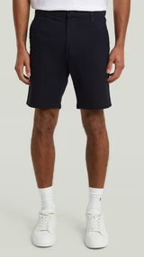 Person wearing navy shorts and white sneakers on a plain background