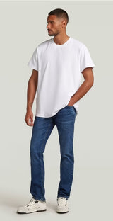 Man wearing a plain white t-shirt and blue jeans on a light gray background