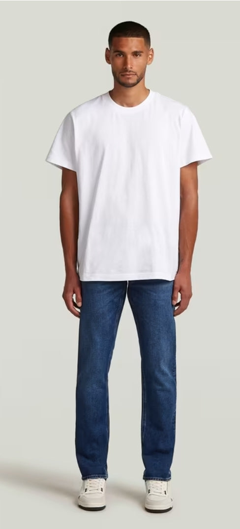 Man wearing a plain white t-shirt and blue jeans on a light gray background