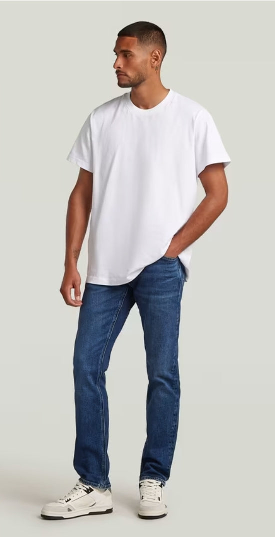 Man wearing a plain white t-shirt and blue jeans on a light gray background