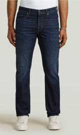 Person wearing dark blue jeans and white sneakers on a light gray background