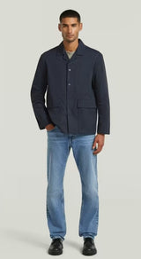 Man wearing a navy jacket and blue jeans on a light gray background